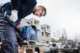 Eine Person mit Sicherheitsausrüstung verwendet eine Motorsäge, um im Freien eine Betonplatte zu schneiden.