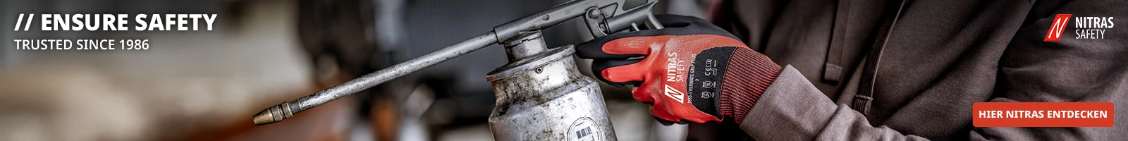 Werbebanner mit dem Logo und der Aufschrift NITRAS Safety links oben. Im Vordergrund eine Person, die eine Ölspritzkanne hält und rote Arbeitshandschuhe trägt. Rechts unten ein roter Button mit der Aufschrift Hier entdecken ...