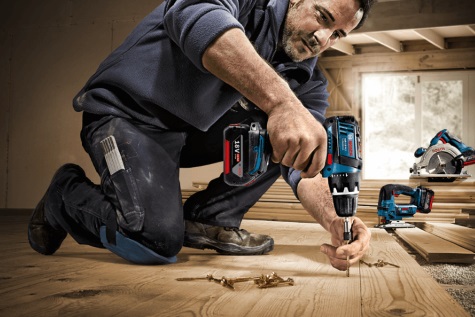 Titelbild Produktgruppe Akkutechnik - Ein Handwerker arbeitet kniend mit einem Bosch Akku-Bohrschrauber an einem Holzboden; im Hintergrund sind weitere Bosch Akkuwerkzeuge und Zubehör in einer hellen Werkstatt zu sehen.