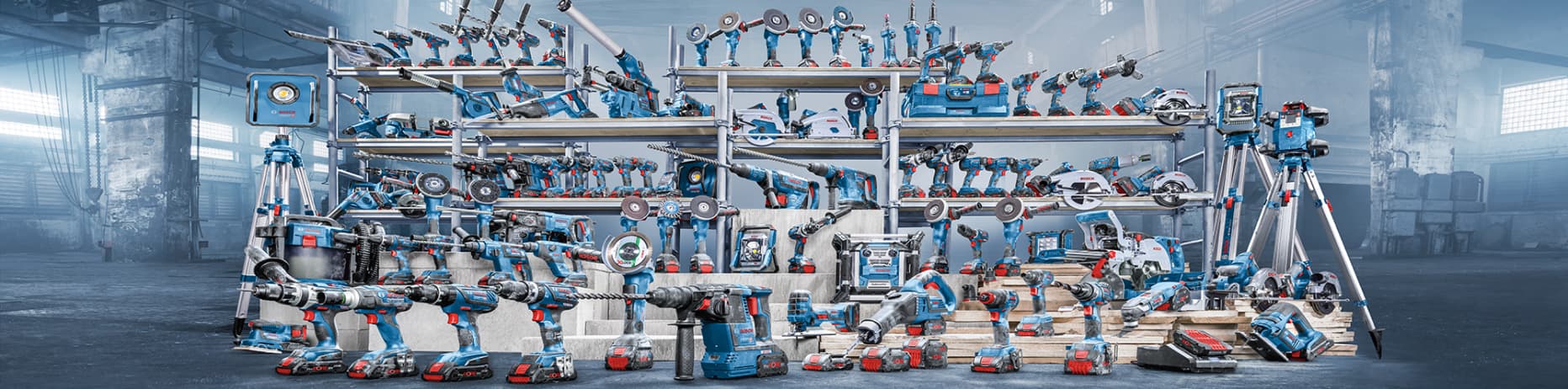 Bild einer großen Werkstattregalwand, voll bestückt mit einer Vielzahl von Bosch Professional Elektrowerkzeugen und Zubehör in Blau mit roten Details. Zu sehen sind u. a. Bohrmaschinen, Akkuschrauber, Winkelschleifer, Sägen, Messgeräte und weitere Geräte, ordentlich in mehreren Regalreihen aufgereiht.